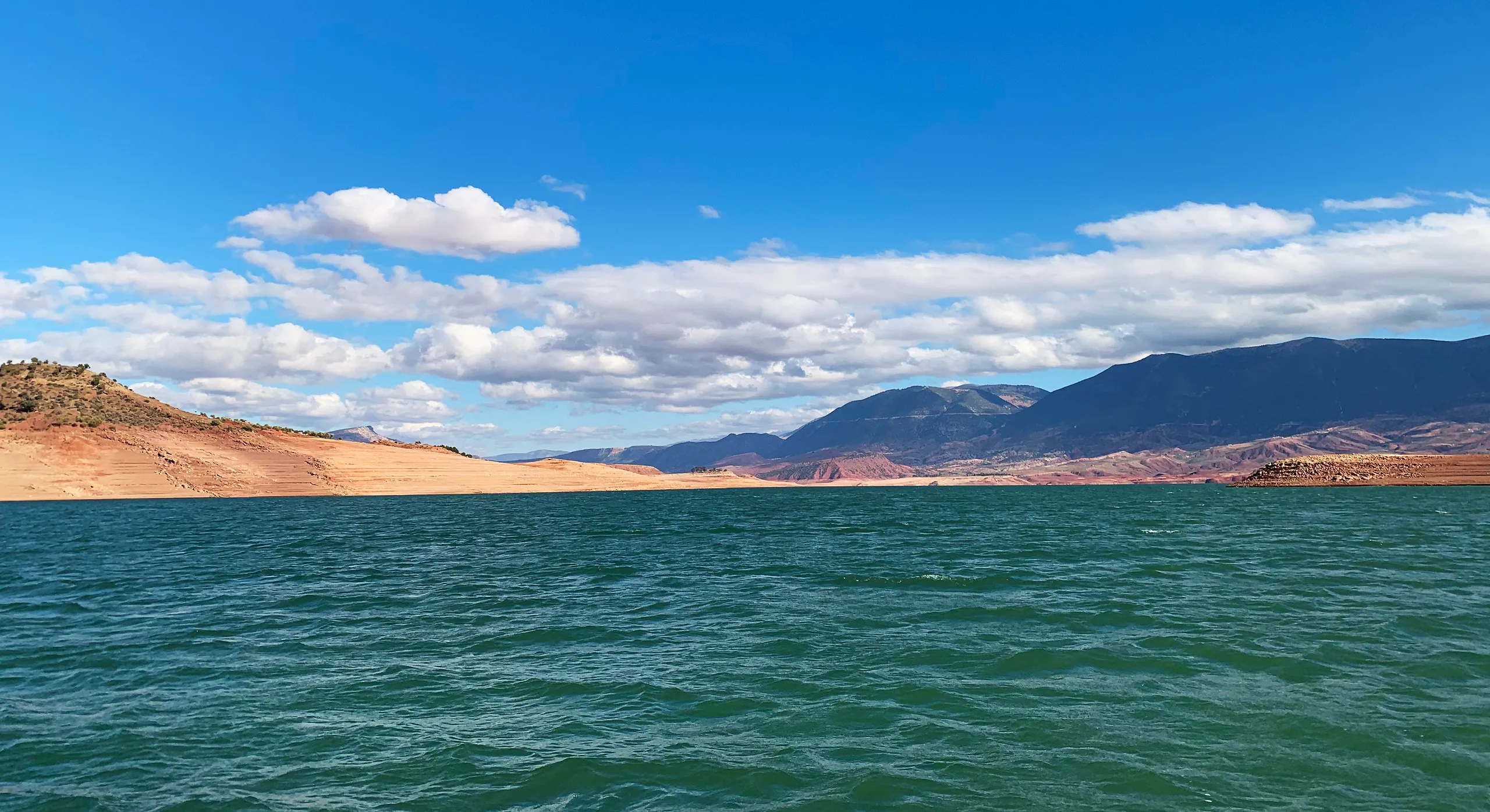 Green water of Bin El Ouidane at paddle height, with red shores and Middle Atlas ridges behind