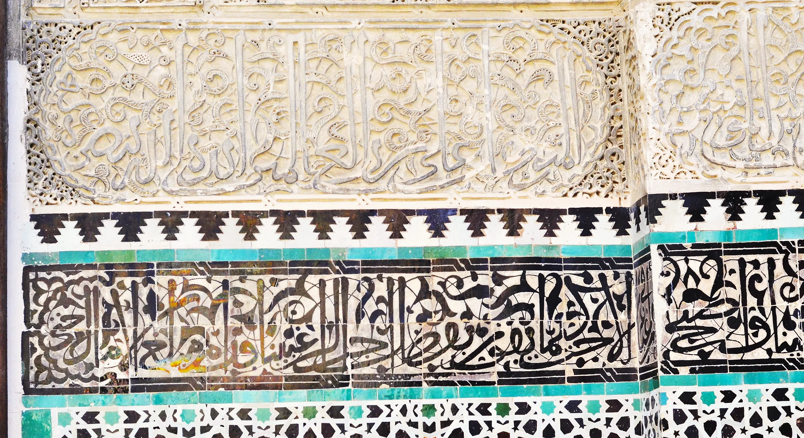 Carved stucco calligraphy above bands of zellige tilework at the Bou Inania Madrasa in Fes
