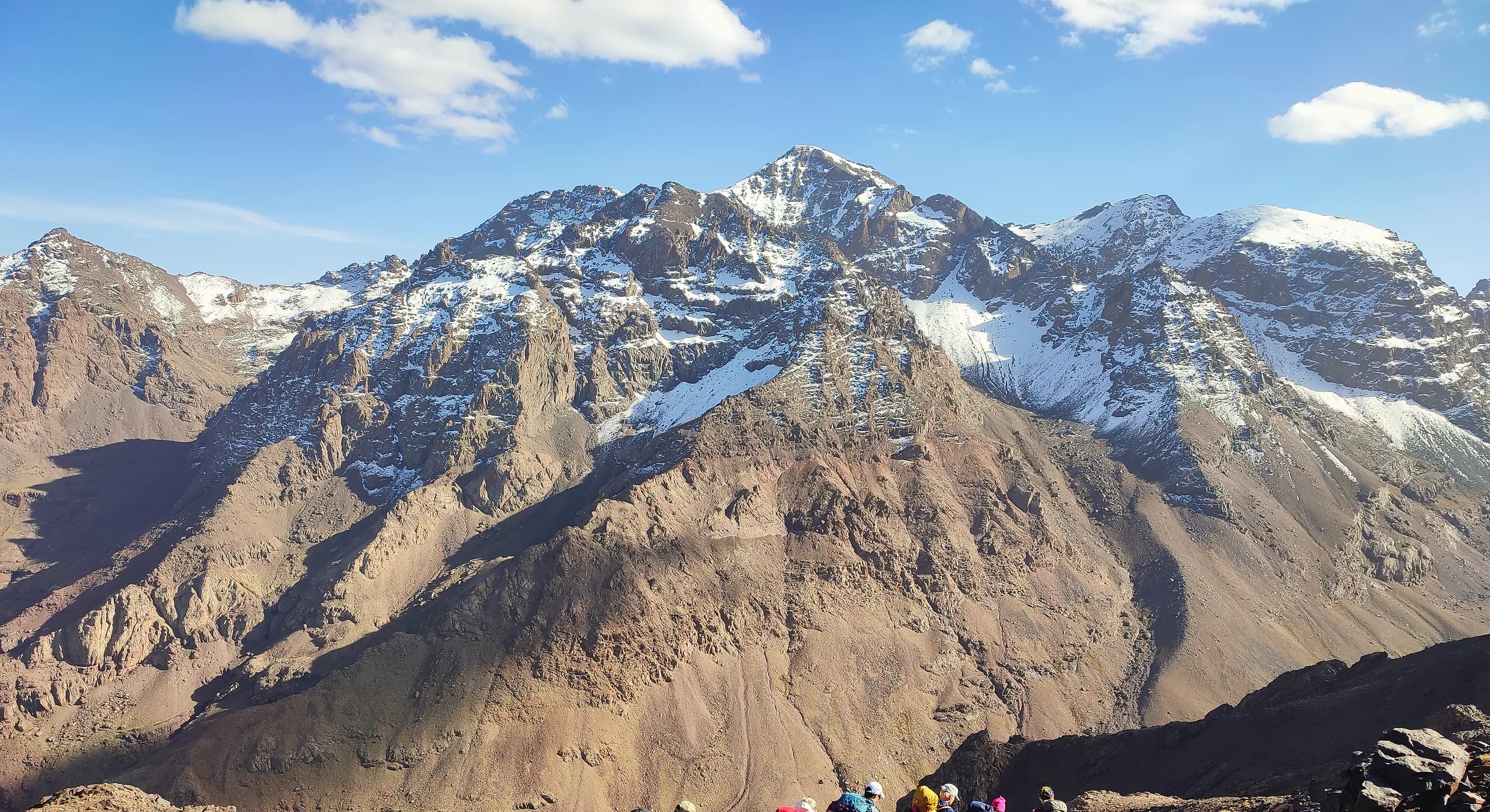 Snow-streaked Jebel Toubkal under a blue sky, with a group of hikers in the foreground