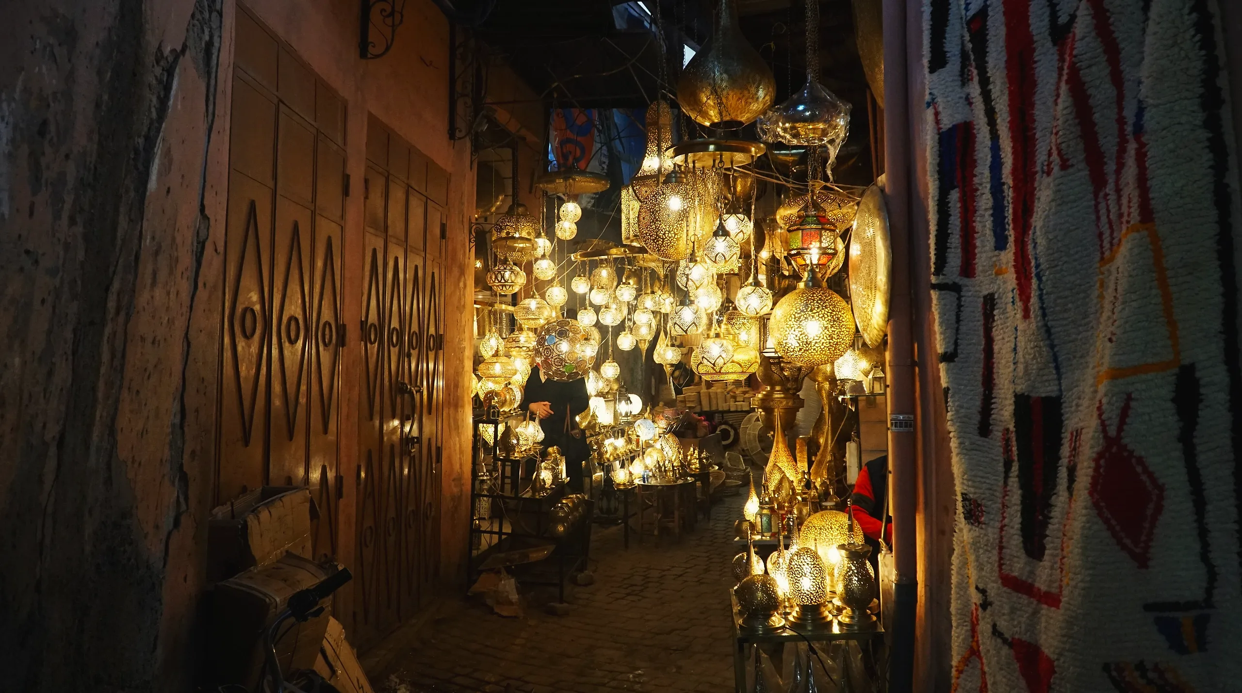 Brass lanterns lit up in a lamp shop along a covered souk alley in Marrakech