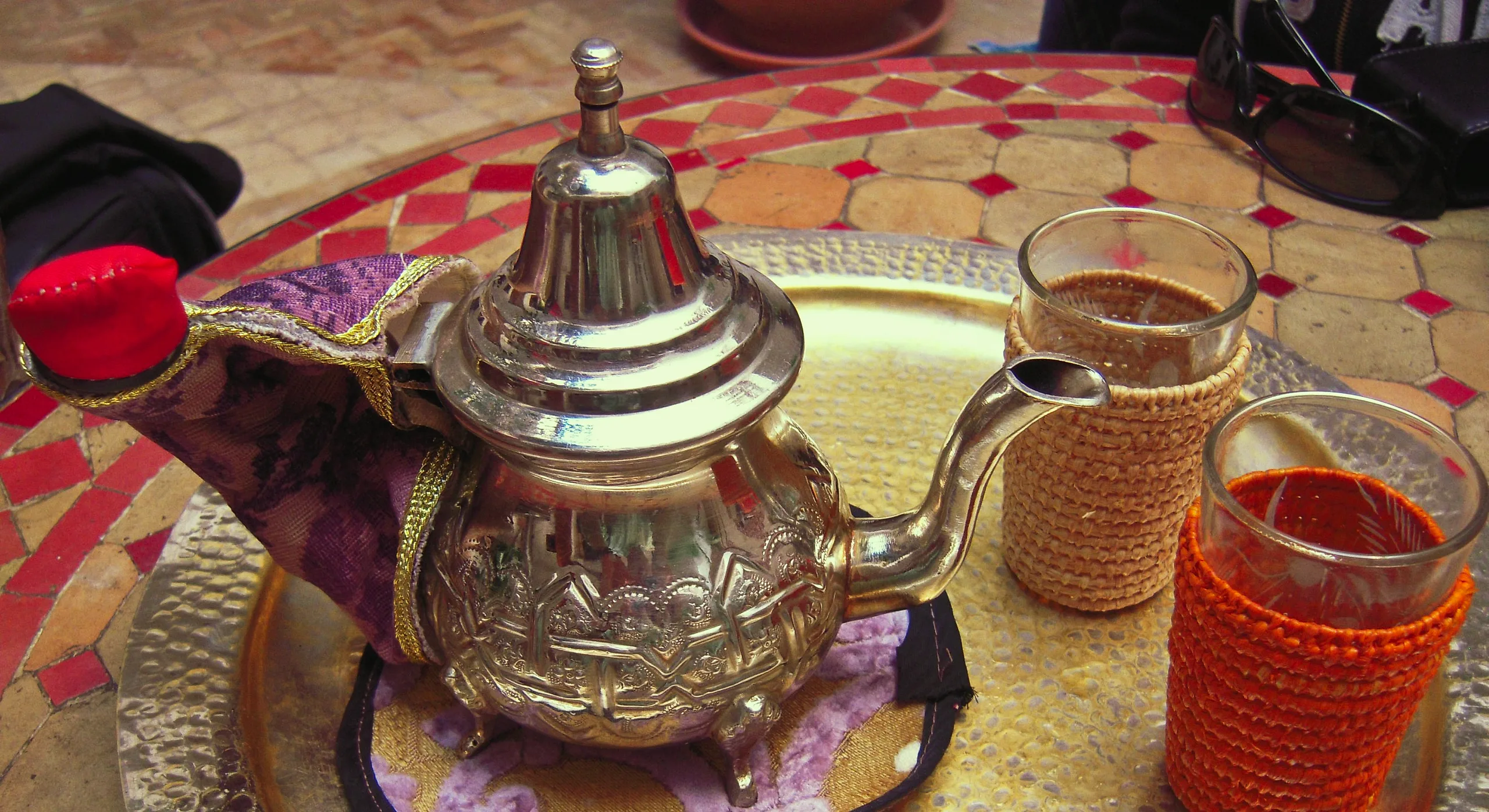 A silver teapot and two glasses of mint tea on a brass tray, on a tiled café table