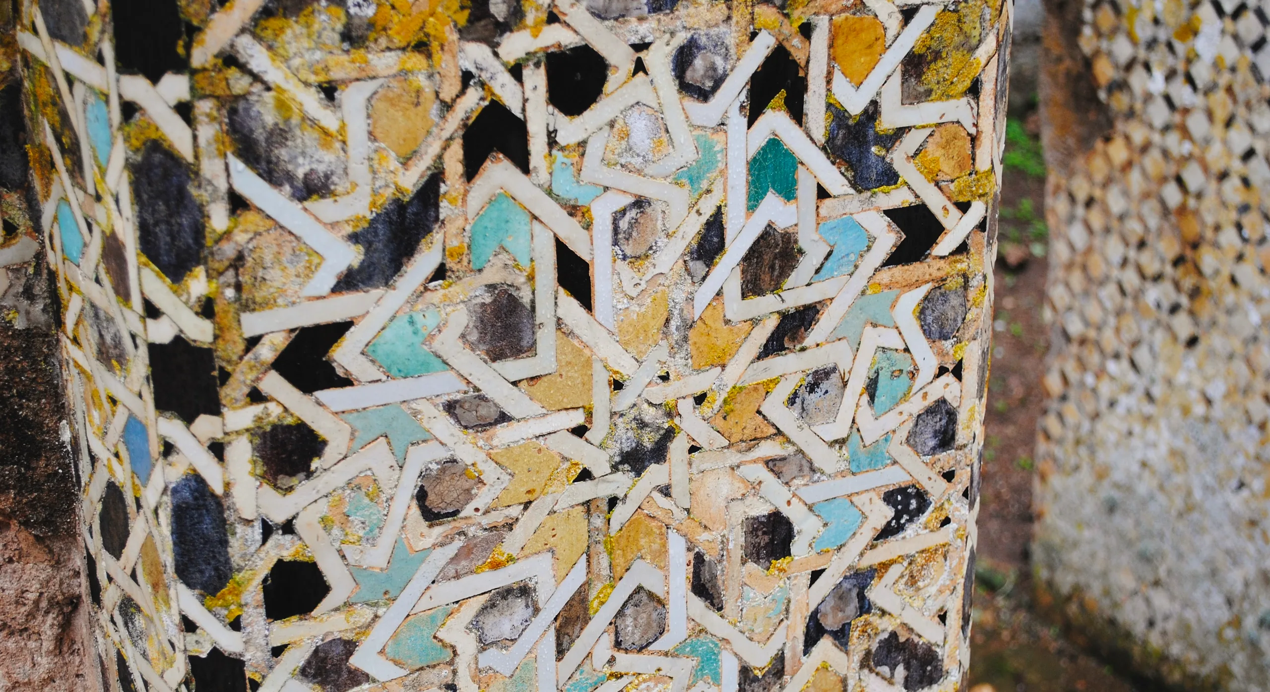 Weathered Marinid zellige in interlacing star patterns, spotted with lichen, at the Chellah, Rabat